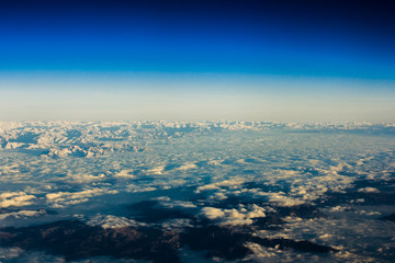 Aerial view from the plane on the panorama of the Alp mountains and hills ridge. Mountain peak of rocks covered by clouds and fog. View from above on mountain landscape.