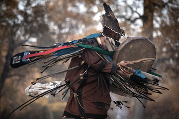 Mongolian traditional shaman performing a traditional shamanistic ritual with a drum and smoke in a forest during autumn afternoon. Ulaanbaatar, Mongolia.