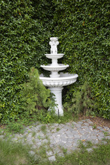 Abandoned white fountain with children cupid sculpture in garden.