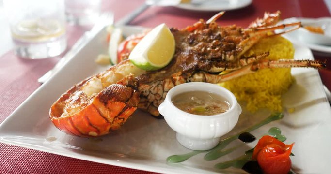 Tasty cooked and grilled lobster, French cuisine with rice and vegetables, lemon and sauce. Caribbean Guadeloupe half lobster grilled on white plate served in a restaurant