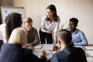 Female mentor teaching diverse employees group analyze paperwork at briefing