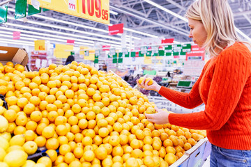 Juicy yellow oranges on a counter in a supermarket. Young woman chooses fruits.