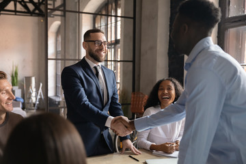 Smiling caucasian businessman handshake african partner at corporate group meeting