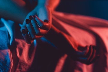 Close up on female young woman's girl's beautiful hands with black nail polish in dark room crossed fingers on the bed sheet gentle passion love temptation emotion love concept - obrazy, fototapety, plakaty