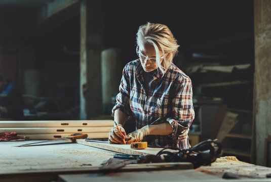 Attractive middle aged woman carpenter designer works with ruler, make notches on the tree in workshop.  Image of modern femininity. Concept of professionally motivated women