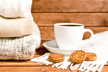 Stack of cozy knitted warm sweater , wooden background . Sweaters in retro Style and a Cup of hot chocolate. The concept of warmth and comfort.