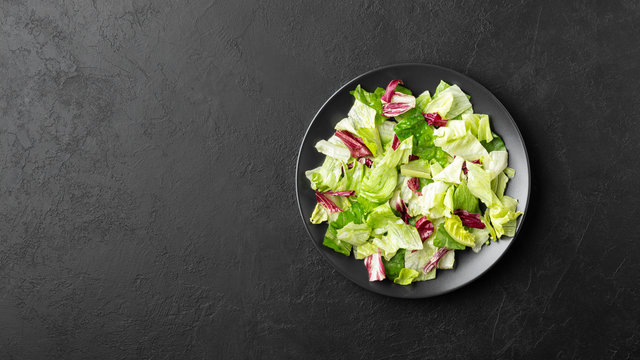 Vegetable salad with iceberg lettuce, romaine and radicchio salad on black background. Healthy food. Top view with copy space.