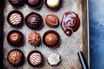 Chocolate candies in a vintage baking dish with chocolatier tool. Close up. Top view.