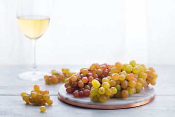 Fresh grape on marble cutting board with glasses of white wine. Wooden background. Copy space.