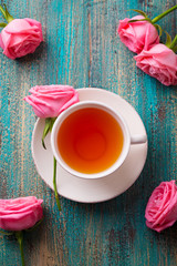 Cup of tea with pink rose. Colorful turquoise wooden background. Top view.