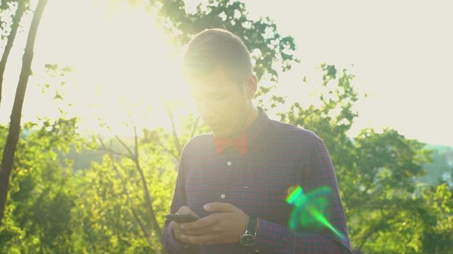 Disturbed surprised young attractive European Caucasian man using his smartphone at amazing beautiful sunset in park urban city background