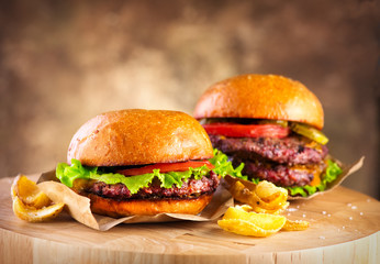 Hamburger and Double Cheeseburger with fries rotated on wooden table background. Cheeseburgers on fresh buns with succulent beef and fresh salad ingredients served with French Fries - obrazy, fototapety, plakaty