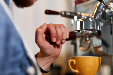 Fototapeta na wymiar Hand of male barista with plaster on finger, keeps tamper on coffee machine, presses hot tasty americano into big beautiful cup, professional concept
