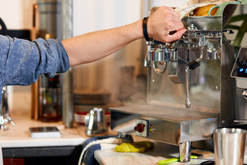 Hand of professional barista keeps handle of grinder tightly, trying to turn with effort, in modern well coffee shop, working place of bartender