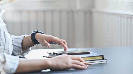 Cropped shot woman touching on her smartphone on desk.