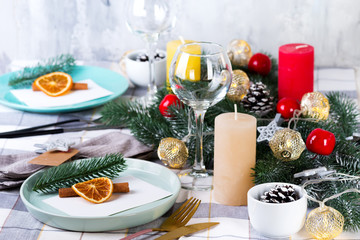 Festive Christmas and New Year table setting with dry orange and cinnamon on a gray textile. Dining place decorated with pine cones, branches and candles