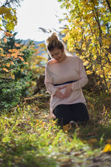 Young pregnant woman in nature enjoying autumn sun outdoors.