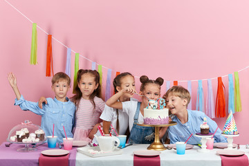 little cute funny girl holding forks , soons going to taste dessert with friends who are standing behind the table, isolated pink background, holiday, festive time