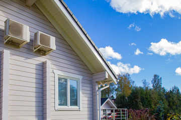 Cottage against blue sky. The beauty of a country holiday. Two air conditioners on the facade of the house. Indoor climate control. Comfort in the house. Installation of air conditioners.