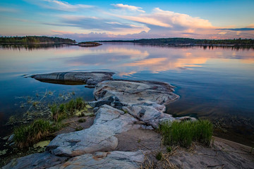 Karelian landscape at sunset. Rocky island goes under the water. Skerries of lake Ladoga. Clouds are reflected in the water of the lake. Nature of Russia.