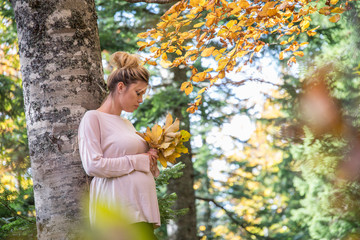 Young pregnant woman in nature enjoying autumn sun outdoors.