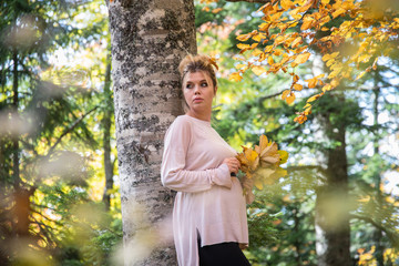 Young pregnant woman in nature enjoying autumn sun outdoors.