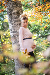 Young pregnant woman in nature enjoying autumn sun outdoors.