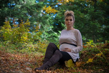 Young pregnant woman in nature enjoying autumn sun outdoors.