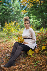 Young pregnant woman in nature enjoying autumn sun outdoors.