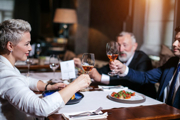 Close up of emotional optimistic woman dressed in white clothes, happily clinking glass of wine with young handsome man