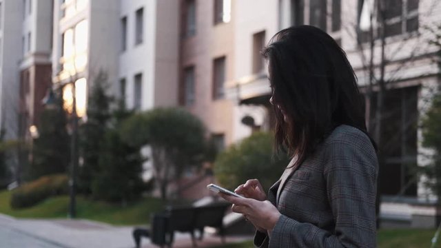Portrait of a confident business woman in a suit uses a smartphone outdoors