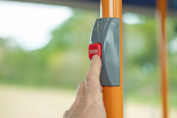 Adult commuter seen pressing a request stop button inside a public transport bus. Seen on a busy commuter day, yellow handrails are also visible in the moving bus.
