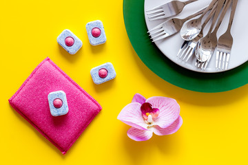 Obraz premium Dry detergent for dishwashing near plates and orchid flower on yellow background top view