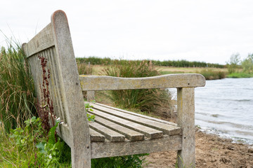 Empty, wooden park bench seen close to a flooded quarry. The water has receded from near the bench itself, causing flooding to the surrounding area