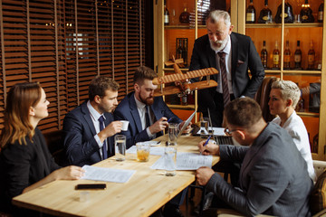 Elderly team leader dressed in business suit demonstrates the layout of helicopter to business partners. Young men carefully studying documentation, business woman watching speaker with interest