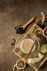Masala tea in glass on wooden background in rustic style. Traditional Indian hot drink with milk, black tea and spices. Copy space, top view, close-up