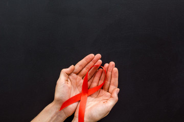 AIDS disease symbol. Red ribbon in hands on black background top view copy space