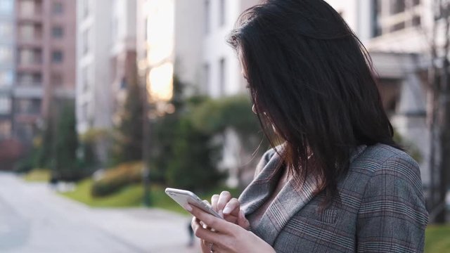 Portrait of a confident business woman in a suit uses a smartphone outdoors