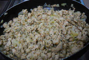 Finely chopped pieces of homemade chicken breast, fried and stewed with onions and sunflower oil. Slices of delicious, juicy chicken lying on a black skillet while frying.