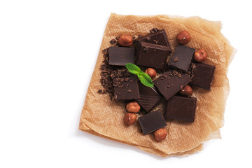 Pieces of dark chocolate, hazelnuts and mint on parchment paper, white background, isolated. View from above,