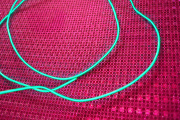 Green glowing wire, cold neon, electroluminescent cord, cable lies on a holographic pink background with various types of overflow.