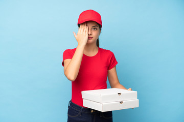 Young woman holding a pizza over isolated pink wall covering a eye by hand