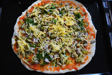 A delicious preparation for Ukrainian pizza with slices of chicken breast, tomato sauce, parsley, cheese located on a black metal hollow.