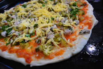 A delicious preparation for Ukrainian pizza with slices of chicken breast, tomato sauce, parsley, cheese located on a black metal hollow.