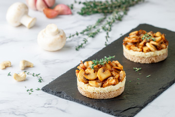 Delicatessen snack for vegetarians (vegans) of fried mushrooms with onions, garlic, thyme and cashew nuts on bread slices. Selective focus