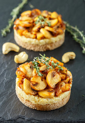 Delicatessen snack for vegetarians (vegans) of fried mushrooms with onions, garlic, thyme and cashew nuts on bread slices. Selective focus