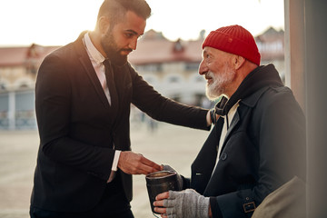 Man in tuxedo came up to beggar to help, give money donation. Rich man hold out his hand with money...