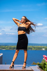 Naklejka premium Portrait of a young beautiful girl in a black skirt and a bra posing on a background of blue sky