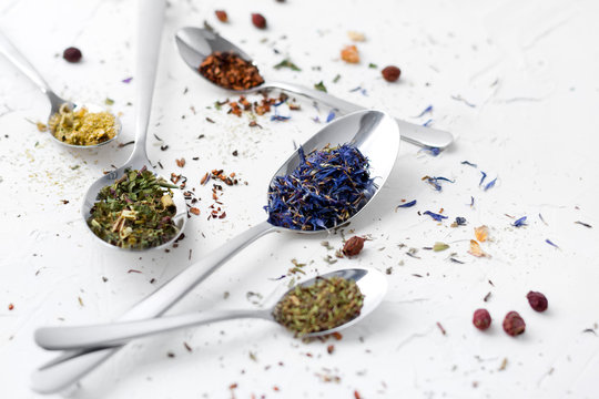 Variety Of Dried Tea, Dried Herbal, Green And Fruit Tea On Spoons Over White Background With Copy Space.