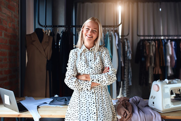 Beautiful caucasian fashion designer stand and happily smile at workplace, look at camera. Dressed in white dress. Background design studio - Powered by Adobe
